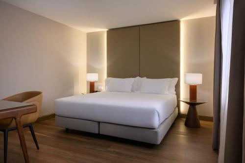 a white bed in a hotel room with two lamps at Hotel Coimbra Aeminium, Affiliated by Meliá in Coimbra