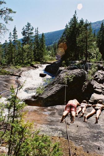 three people laying on rocks near a river at Koselig leilighet i Austbygde med Wifi in Bakko