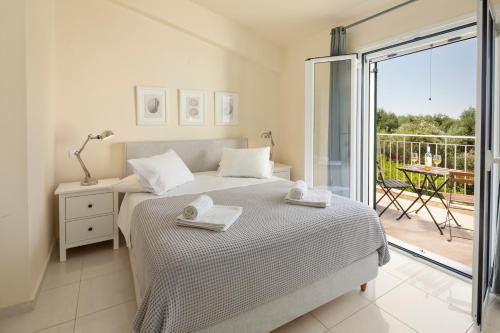 a white bedroom with a bed and a balcony at Skales Villas in Almiros Beach