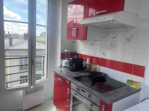 eine Küche mit roten Schränken, einem Waschbecken und einem Fenster in der Unterkunft Appartement à Paris in Le Raincy