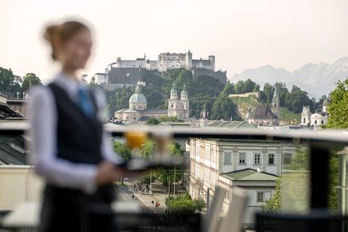 a woman standing on a balcony with a castle in the background at IMLAUER HOTEL PITTER Salzburg in Salzburg