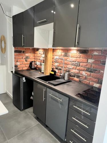 a kitchen with black cabinets and a brick wall at Apartament Bronowice 2 in Kraków
