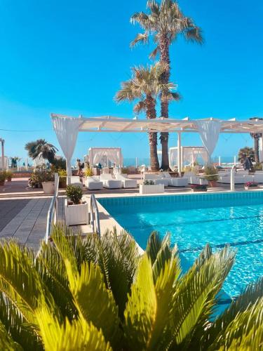 a swimming pool with palm trees and a white canopy at Hotel Mediterraneo in Lido di Latina 