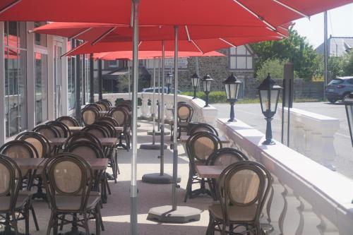 a row of tables and chairs with red umbrellas on a sidewalk at Domaine du Limonay, The Originals Collection in Saint-Méloir-des-Ondes