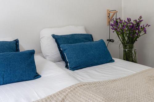 a white bed with blue pillows and a vase of flowers at Lodge Boomklever Nunspeet Veluwe in Nunspeet