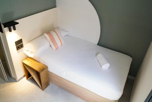 a small bedroom with a white bed with a wooden table at Coliving Compostela in Santiago de Compostela