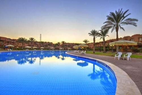 a large blue swimming pool with chairs and palm trees at Royal Chalet Sea View - Stella Di Mare - Families in Az Zafarani