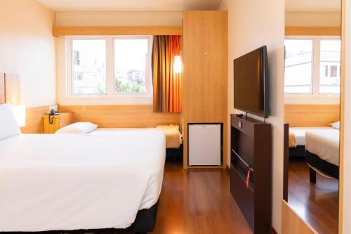 um quarto de hotel com duas camas e uma televisão de ecrã plano em ibis Porto Alegre Moinhos de Vento em Porto Alegre