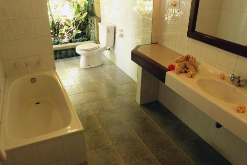 a bathroom with a tub and a toilet and a sink at Klub Kokos Bungalows in Ubud