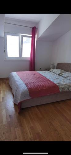 um quarto com uma cama com um cobertor vermelho e 2 janelas em Laki&Uki em Herceg Novi