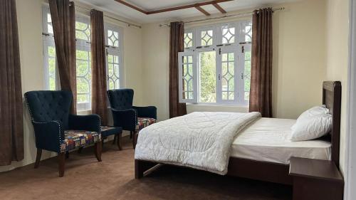 Taaj Residence Skardu في سكردو: غرفة نوم بها كرسيين وسرير ونوافذ