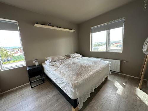 um quarto com uma cama com lençóis brancos e 2 janelas em Apartment Lyngas - Birta Rentals em Garðabær