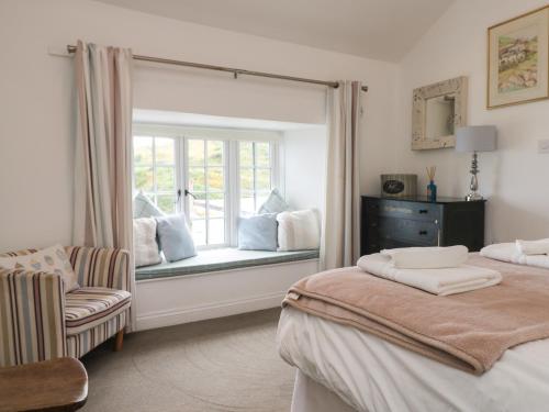 a bedroom with two beds and a window with a chair at Kerbenetty Harbour Cottage in Portloe