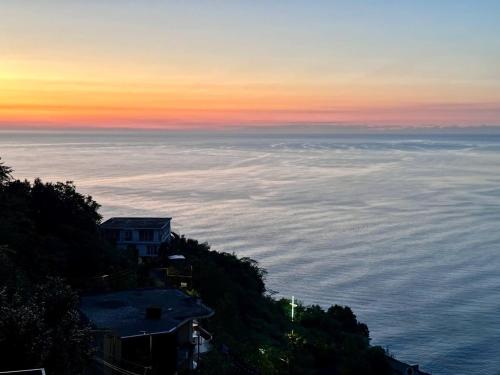 a sunset over the ocean with a house on a hill at Goga Guest House in Kvariati
