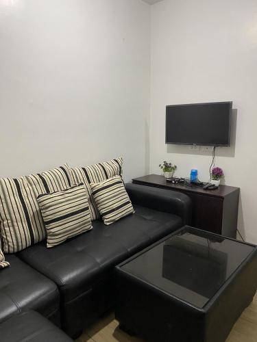ein Wohnzimmer mit einem schwarzen Sofa und einem Flachbild-TV in der Unterkunft Alitheia Condo @ Pine Suites Tagaytay in Tagaytay