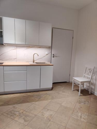 a kitchen with white cabinets and a sink and a chair at apartament 2 pokoje in Kamień Pomorski