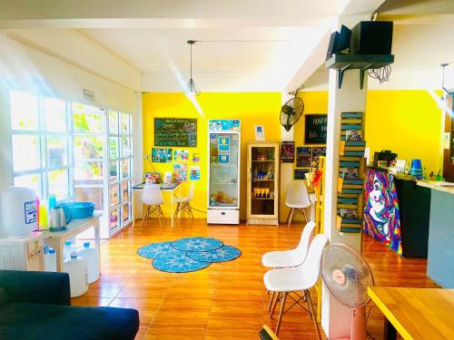 una sala de estar con paredes amarillas y sillas blancas. en See Sea Backpackers House, en Baan Tai