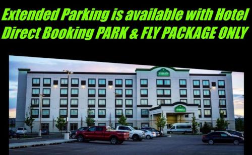 een groot wit gebouw met auto's geparkeerd op een parkeerplaats bij Wingate by Wyndham Calgary Airport in Calgary