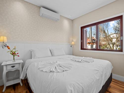 1 dormitorio con 1 cama blanca y ventana en Solar Encantado, en Gramado