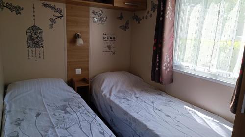 two beds in a small room with a window at Mobil home 3 ch domaine de kerlann pont aven wifi inclu in Pont-Aven