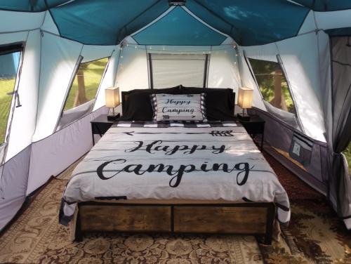 a bed in a tent with a happy camping sign on it at Glamping on the Green River in Washago