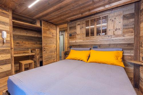 a bedroom with wooden walls and a bed with yellow pillows at ValmalencoAlpina in Caspoggio