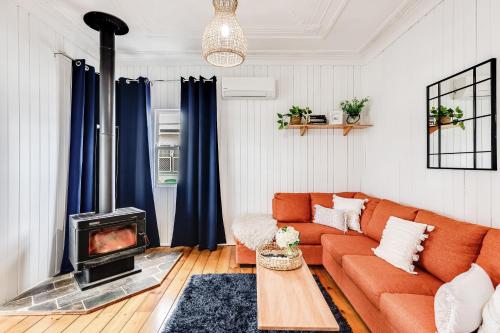 a living room with an orange couch and a fireplace at Cheerful, Cosy Cottage - Near Rose Garden! in Toowoomba