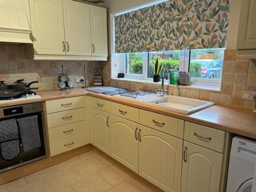 a kitchen with white cabinets and a sink and a window at Tennyson House - 3 Bedroom House for Families, Business Travellers, Contractors, Free Parking & Wifi, Nice Garden in Royal Wootton Bassett