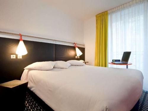 a large white bed in a hotel room with a laptop at ibis Styles Paris République Le Marais in Paris