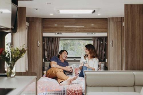 dos personas sentadas en una cama en una caravana en Reflections Byron Bay - Holiday Park, en Byron Bay