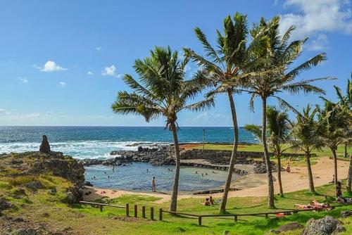 a beach with palm trees and people in the water at Hotel Hanau'eepe in Hanga Roa