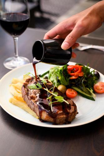 a person pouring a bottle of wine onto a plate of food at Rendezvous Hotel Perth Scarborough in Perth