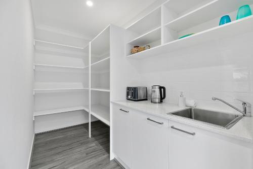 uma cozinha com armários brancos e um lavatório em OSPREY ISLAND RETREAT em Banksia Beach