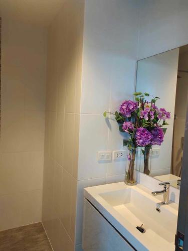a bathroom with a sink with a vase of purple flowers at GrandBlue Condo 102 by malai in Mae Pim
