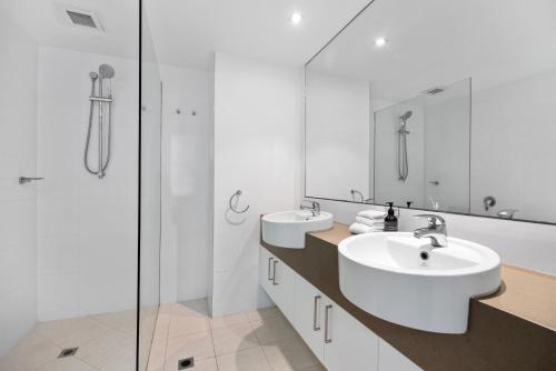 a white bathroom with two sinks and a shower at Fairshore 12: Absolute Beachfront, Direct Beach & Pool Access in Noosa Heads