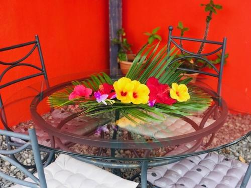 a glass table with flowers on top of it at Location Villa pleine Nature Domaine des Radiers in Sainte-Rose