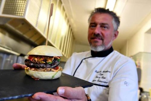 a chef holding a large sandwich on a cutting board at Logis Relais des Monedieres in Seilhac