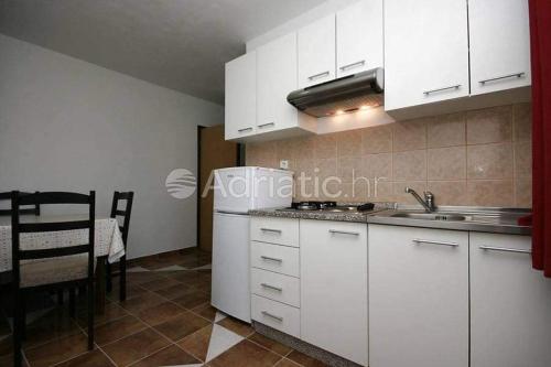 una cucina con armadi bianchi, lavandino e tavolo di Apartments Zoran a Povljana (Pogliana)