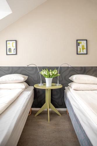 two beds with a table with a vase of flowers on it at Hotel Kupolen in Borlänge