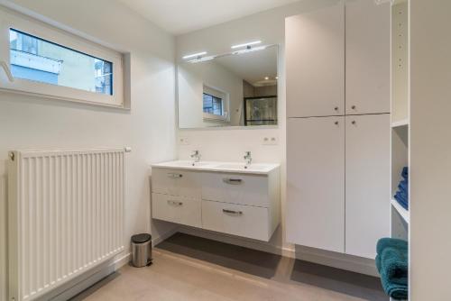 a white bathroom with a sink and a mirror at Maison les Bruyères in Blankenberge