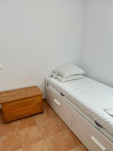 a white bedroom with a bed and a wooden table at Acogedora casita en Mugardos. in Mugardos