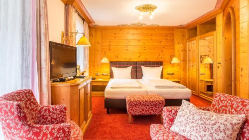 a bedroom with a bed and two chairs and a television at Alpenhotel Oberstdorf - ein Rovell Hotel in Oberstdorf