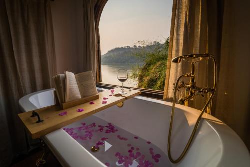 a bathroom with a bath tub with a window and a glass of wine at Ock Pop Tok Mekong Villa in Luang Prabang