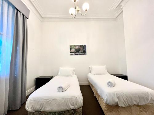 two beds in a room with white walls and a window at Victorian Terrace in the heart of it all! in Melbourne
