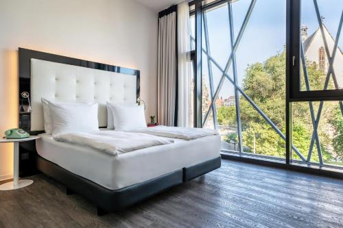 a bedroom with a white bed with a large window at INNSiDE by Meliá Leipzig in Leipzig