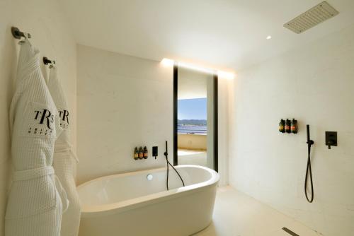 a white bathroom with a tub and a mirror at TRS Ibiza Hotel - Adults Only in San Antonio
