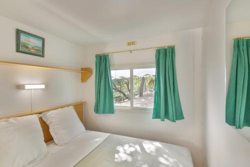 um quarto com uma cama e uma janela com cortinas verdes em Camping du Grand Batailler em Bormes-les-Mimosas
