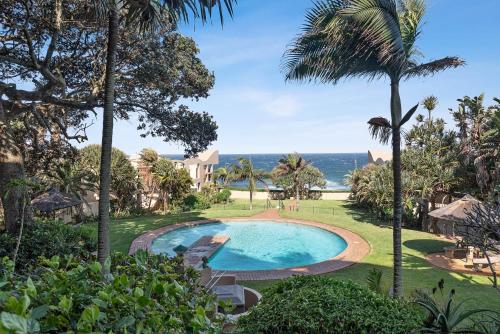 an outdoor swimming pool with palm trees and the ocean at Stylish Beachscape in Umdloti in Umdloti