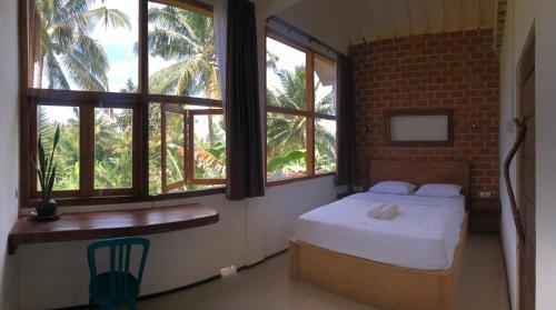 a bedroom with a bed and windows and a chair at Mu Homestay in Tetebatu