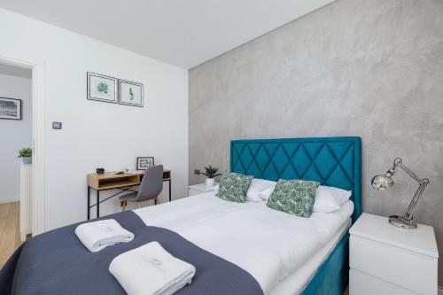 a bedroom with a bed with a blue headboard and a desk at Osiedle Życzeń Apartment Stawowa Cracow by Renters in Krakow